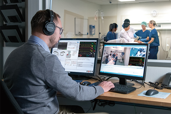 man in simulation control room monitoring students inside simulation room