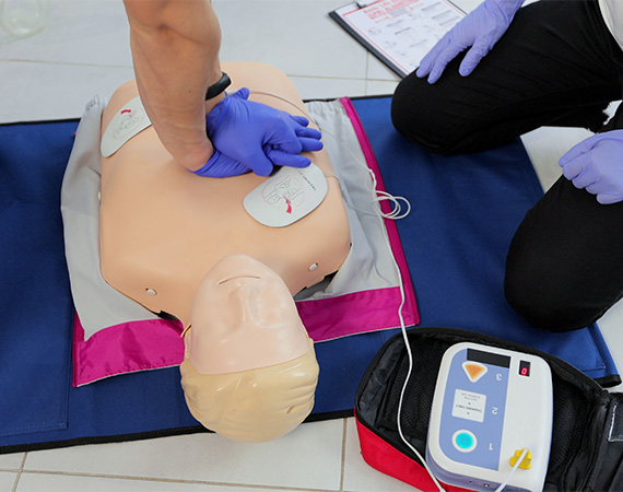 Person performing CPR on Little Anne CPR manikin, using WNL Practi-Trainer AED Trainer and electrodes