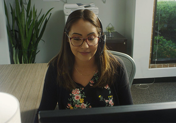 Latina customer service woman seated at computer, wearing headset