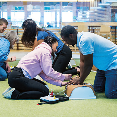 Male student performing CPR on Little Anne manikin while female student applies AED pads